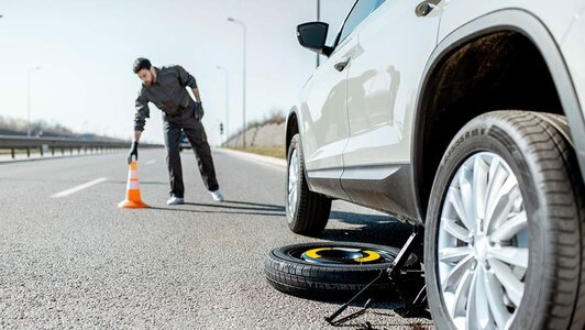 Driver places a safety cone while changing a flat tire on the roadside.