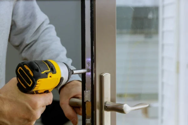 Person using a cordless drill to install or tighten screws on a metal door lock mechanism